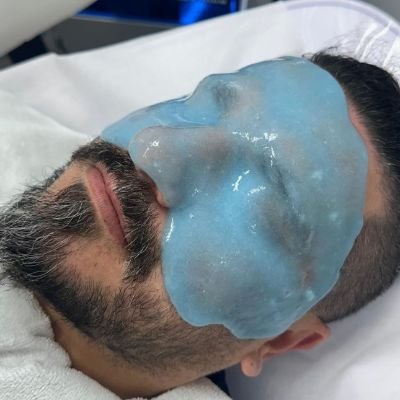 Man receiving a facial treatment with a blue gel mask.