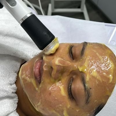 Woman receiving an intensive hydration facial treatment with yellow gel mask.